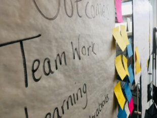 Large white paper attached to the wall with team work written on it and post it notes to the side